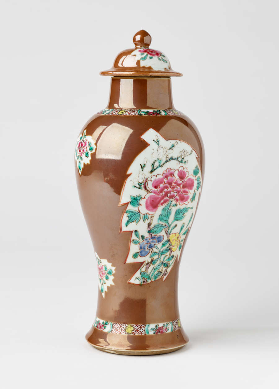 A brown and white covered vase with pink, green, blue, and yellow floral decorations.