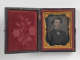 An open black case with a rose imprint in red velvet on the left side, and an orange framed black and white portrait of a man in a suit and bowtie on the right.