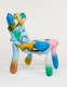 Side view of a four legged chair made of candy colored shapes that mimic balloons. The form is abstract and fluid, evoking a sense of buoyancy despite the hard material.