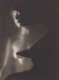 A dreamy black-and-white photograph of a nude female figure, softly lit from the left side, overlapped from the right side with an extended shadow of her profile, breast, and torso. 