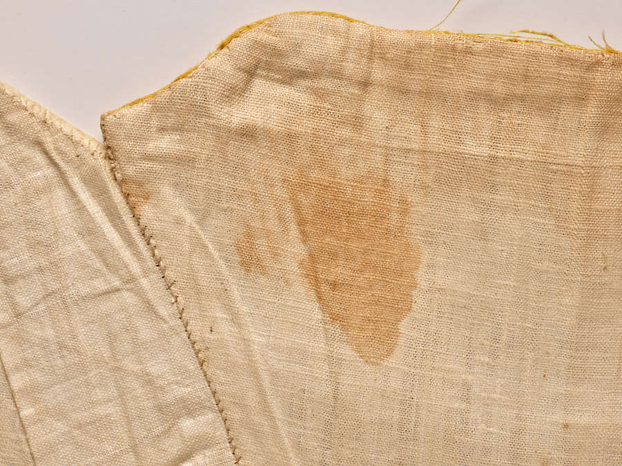 Close-up photo of off-white fabric and seams. At the center is a faint dark stain.