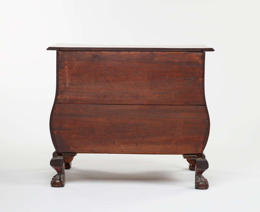 Rear view of a wooden dresser with a plain back panel and curved sides supported by decorative clawed feet.