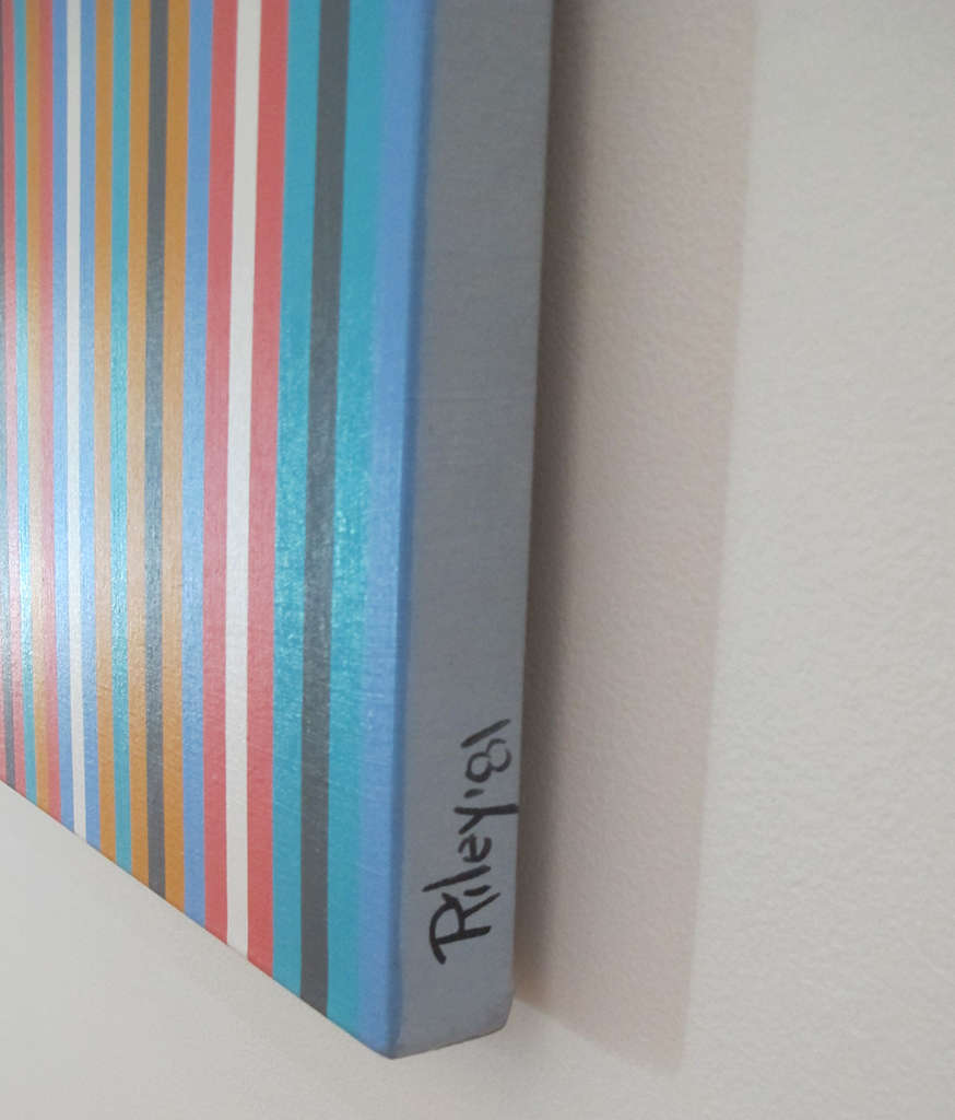 Angled view of a striped painting featuring narrow vertical bands in bright blue, black, red, white, and yellow. The canvas edge is painted grey and signed “Riley ‘81.” 