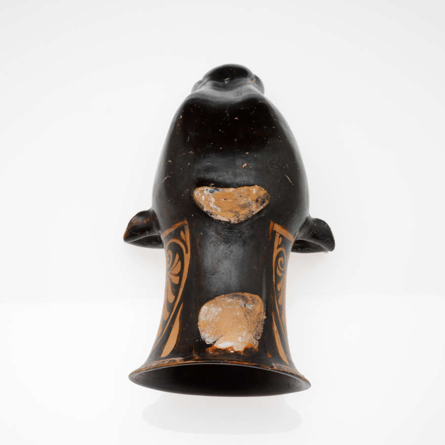 Back view of a black and terracotta cup with a sculpted cow’s head as its base, extending into the cup’s body. Its backside is mostly black, with some wear.