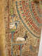 A section of a painted coffin with detailed geometric patterning in red, blue, and gold, above illustrations of symbols and animals.