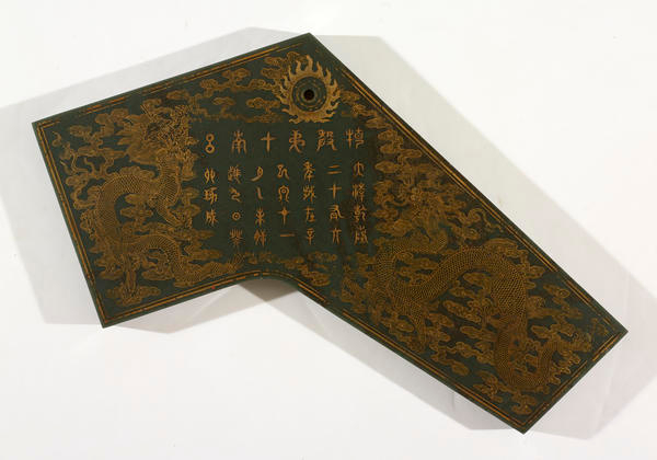 Angular dark green slab ornamented by intricate golden embellishments which depict vertical rows of Chinese characters surrounded by dragons on a backdrop of dense interconnected clouds.