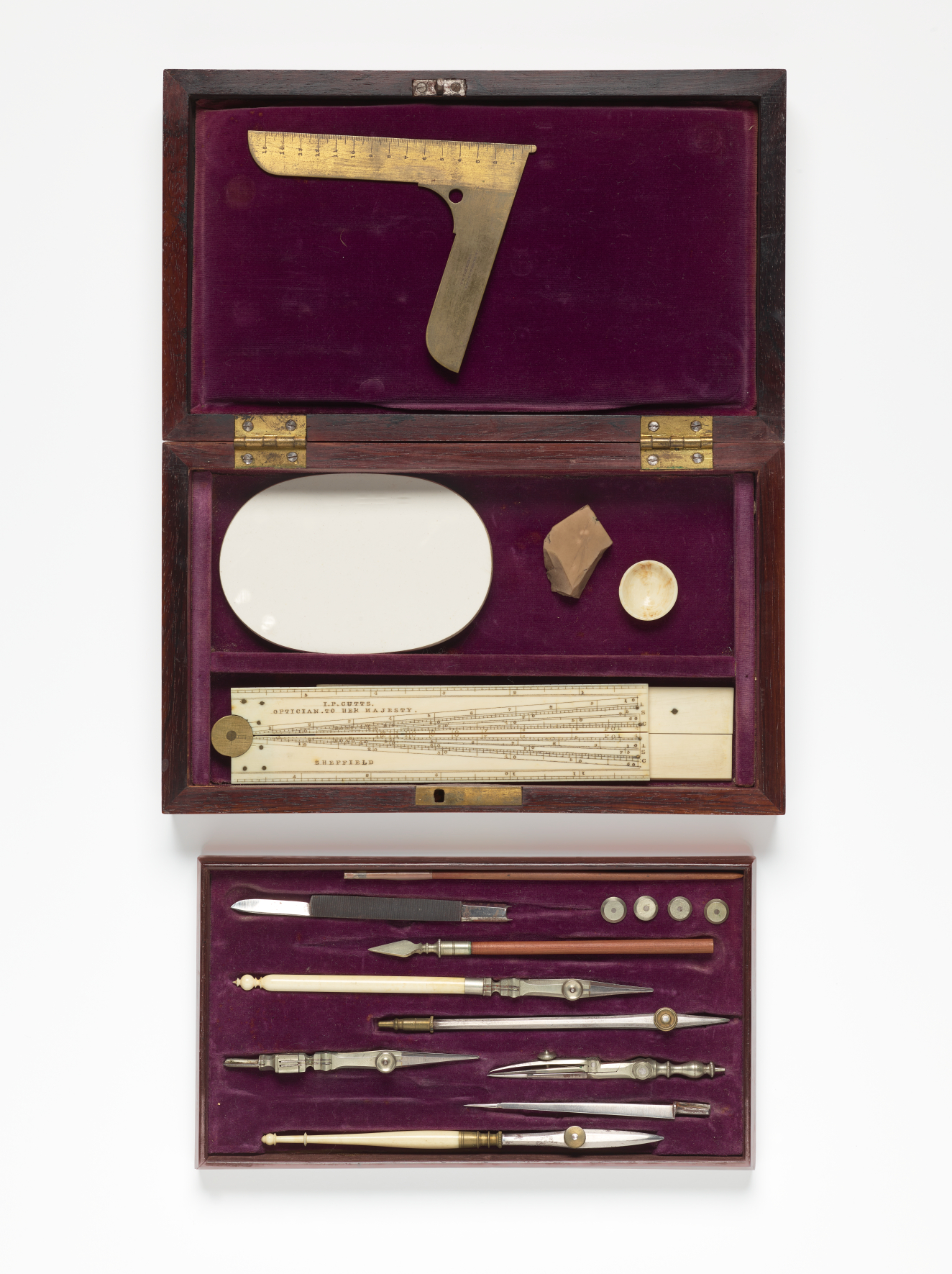 An opened wooden box with purple velvet lining and multiple compartments displaying neatly arranged fine brass and ivory tools including compasses, rulers, and various drawing tools. 
