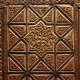 A close up of a wooden panel featuring an intricate central star design surrounded by geometric shapes and floral elements, enclosed by ornate edging.