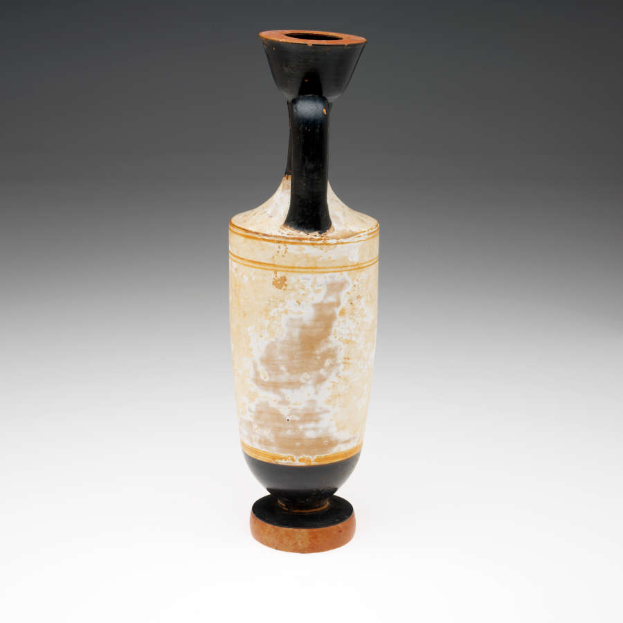 Terracotta vase with a fluted neck, wide mouth, thick foot and handle painted black, with a worn white body. Visible are remnants of yellow decorative patterns and illustrations.