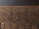 A close-up of an intricately carved wooden panel with repeating X-shaped motifs and ornamental flourishes. 