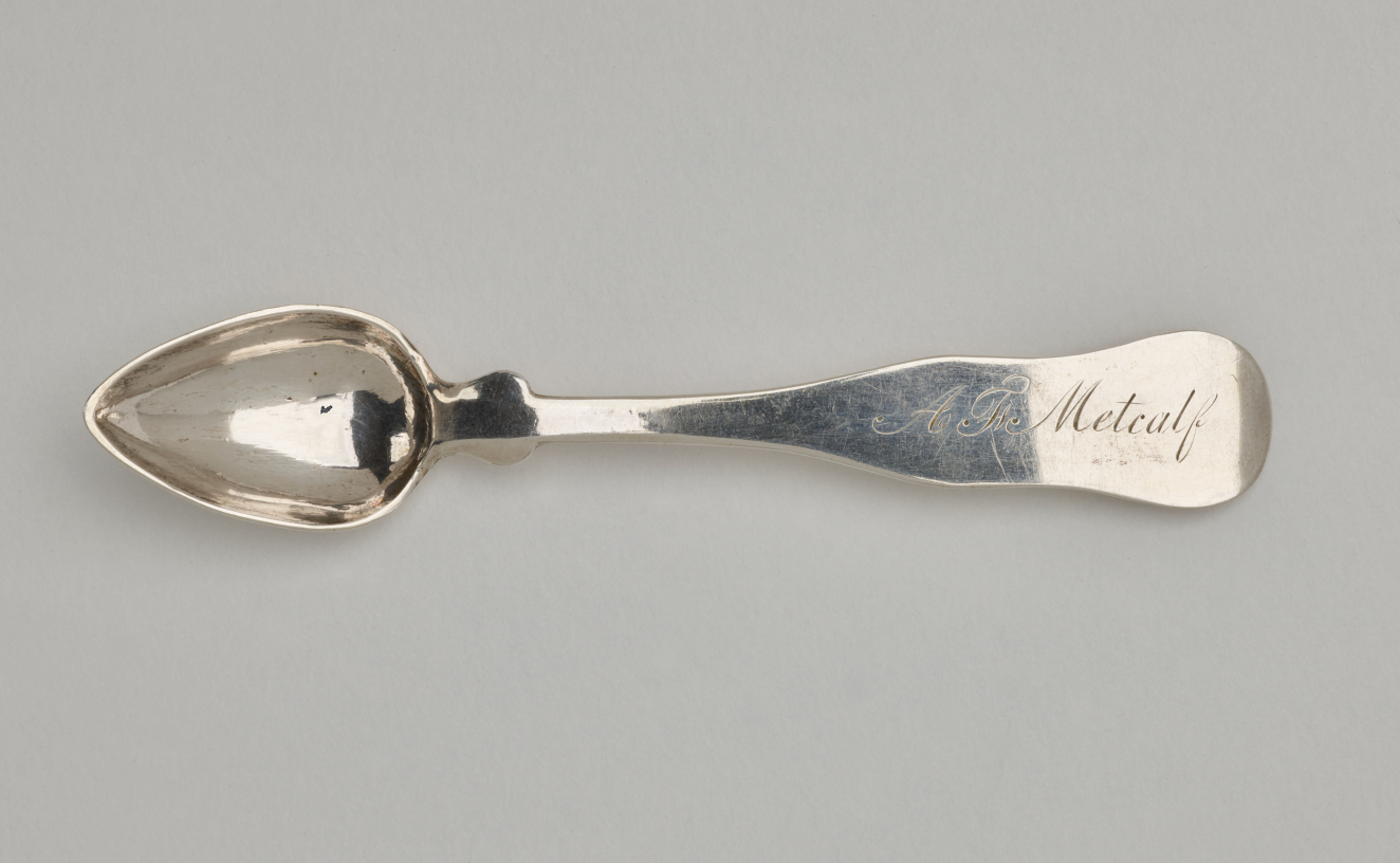 A silver salt spoon the bowl comes to a pointed tip, the neck is thin, and the handle is thicker and rounded at the end.
