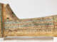 Side view of a coffin's foot, decorated with painted hieroglyphs and a painted depiction of a small reclining sphinx figure by the base.