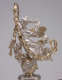 Silver-robed figure with flowing hair and gold wings holds a garland aloft with one cherub holding the end of the garland and the other blowing a horn atop an orb.