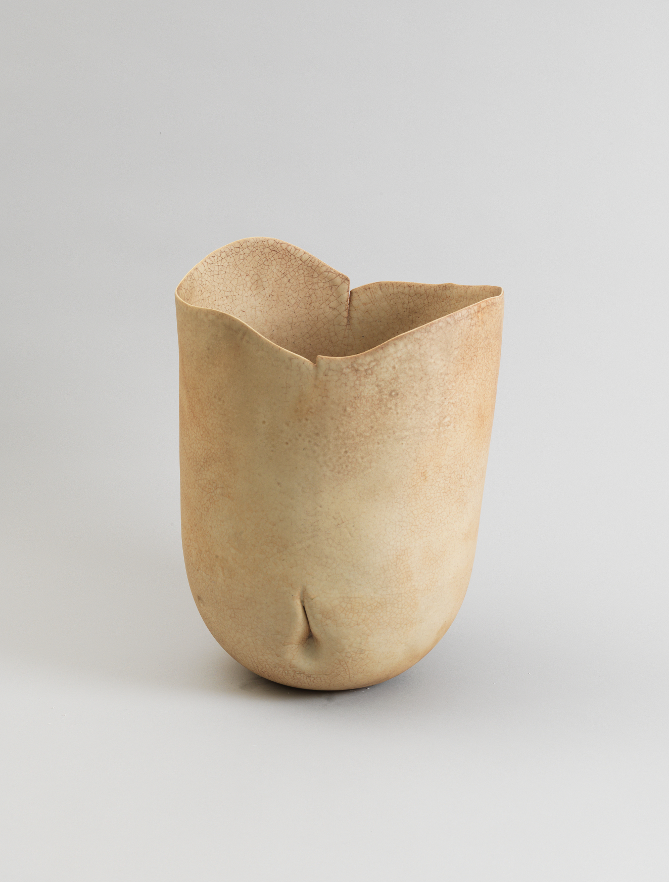 Cream-colored ceramic vessel with soft organic curves and an uneven rim resembling soft folds, marked by a single delicate dimple along the rounded base that suggests an abstracted human torso.