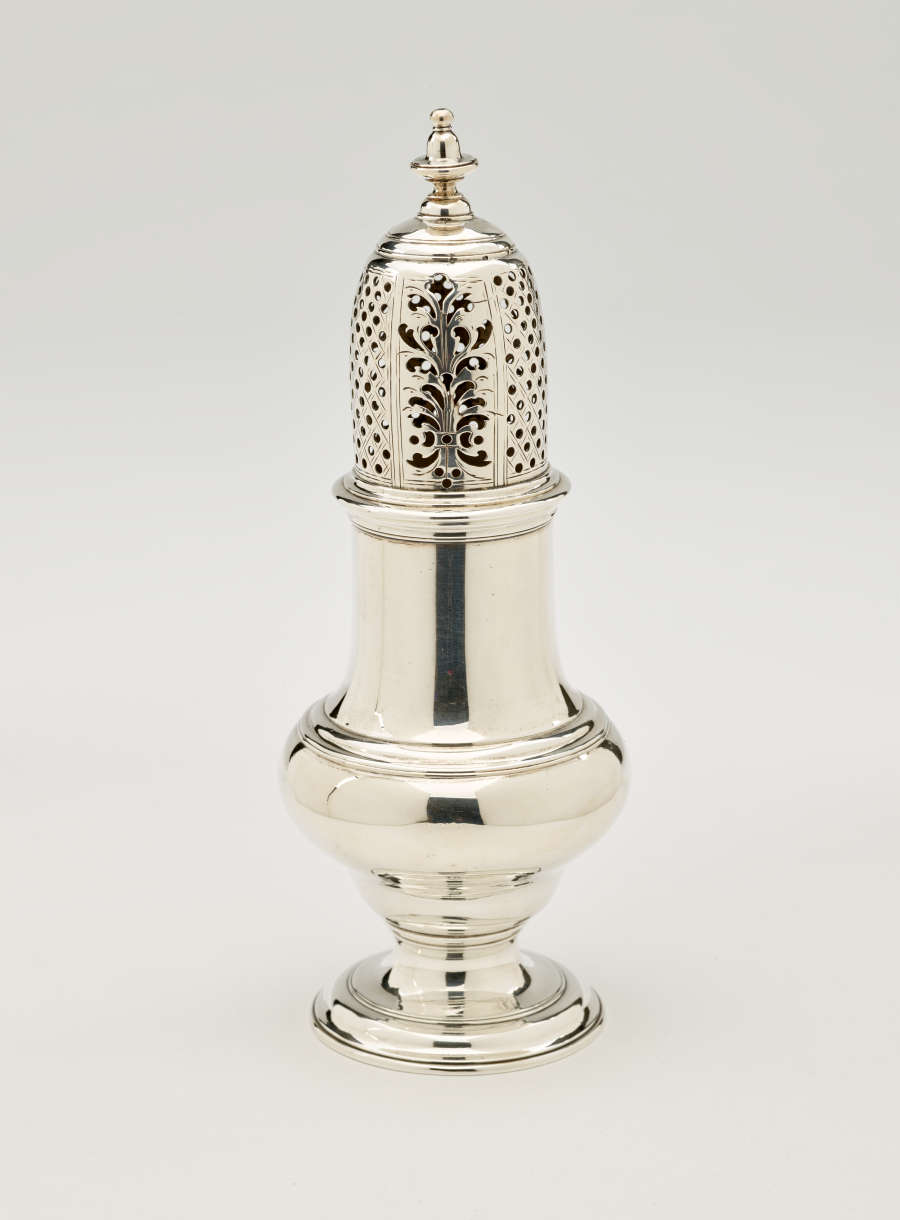 A silver vessel with a foot, rounded body that goes to a cylindrical top half, and the lid is perforated with small holes and floral cutouts.