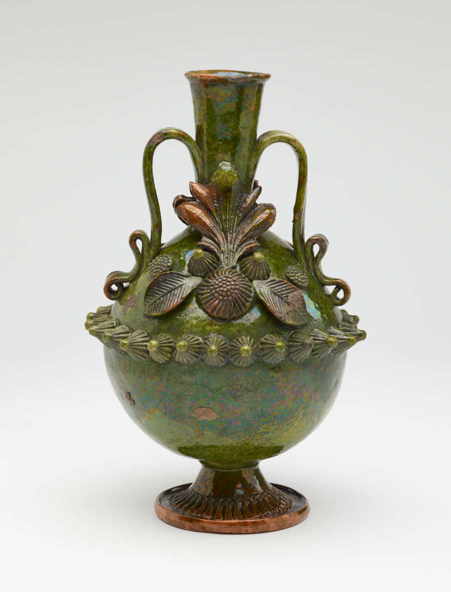 A dark green jug with sculpted decorations, symmetrical decorative handles, and a foot.