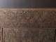 A close up of an intricately carved wooden panel with interlocking triangles and floral details, set within a decorative rectangular border.