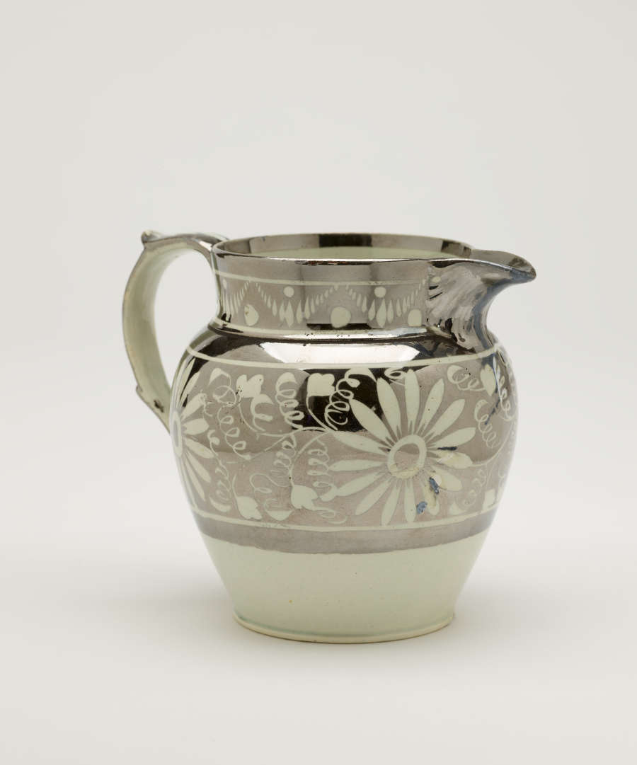 A silver-colored jug with floral motifs on the body of the vessel.