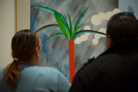 Two people looking at a painting of a palm tree