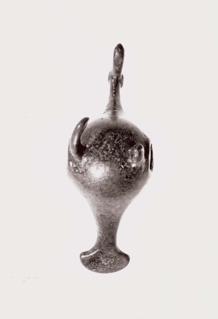 Bottom view of a silver figurine of a bird, with a large round bellow and thin slender neck, and tail that narrows and flares outwards. 