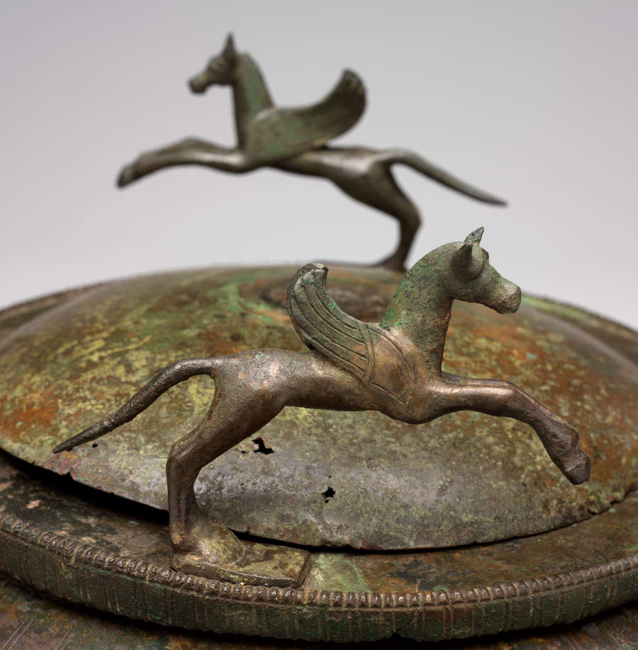 Detail of the bowl’s bronze corroded lid, bringing into focus the black and green patina as well as two of the four bronze winged horses. 