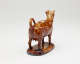  A brown sculptural creamer in the shape of a cow with horns. There is a small flat lid in the center of its back.