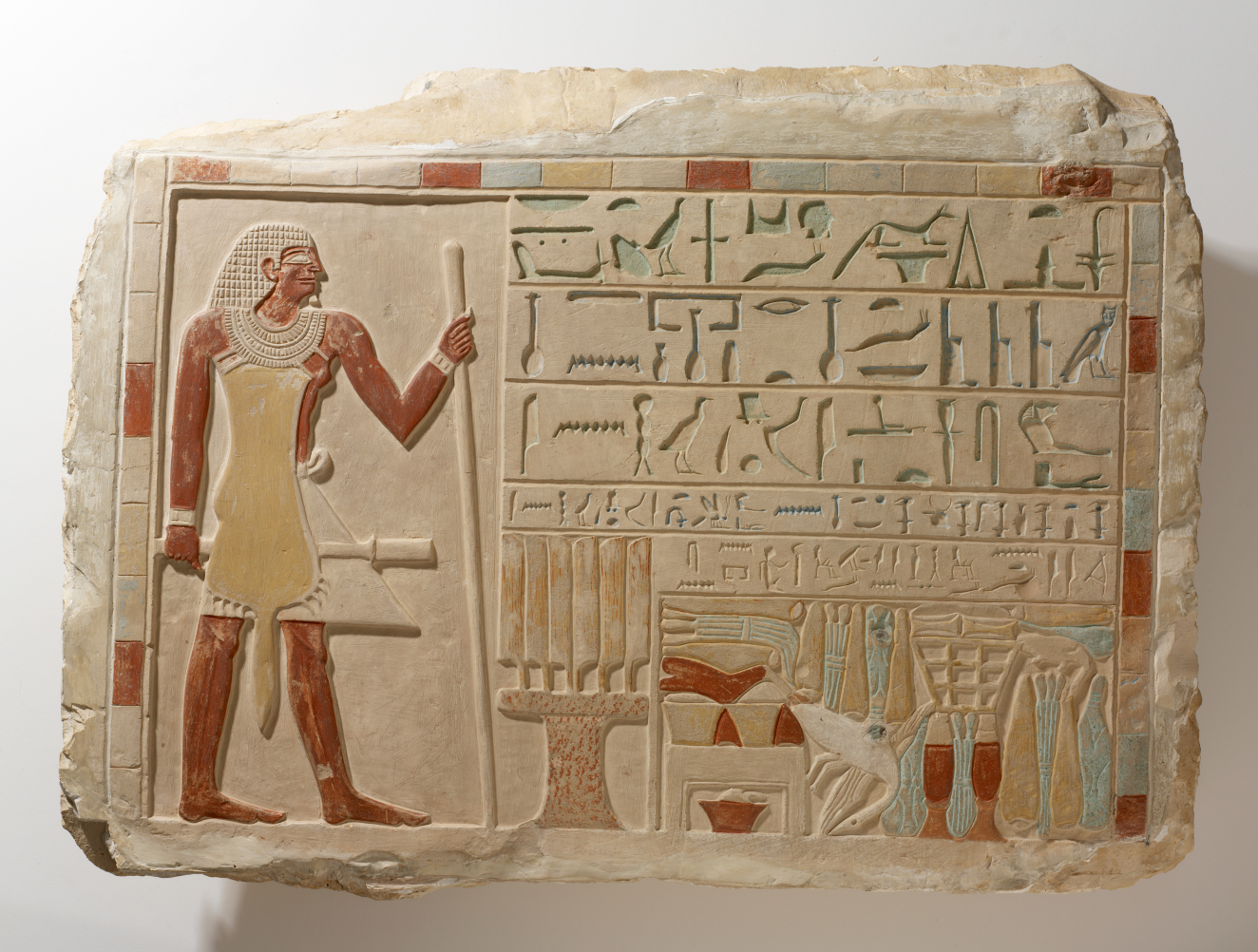 A carved and painted stone slab depicting an Egyptian nobleman in profile, surrounded by hieroglyphs and objects. 