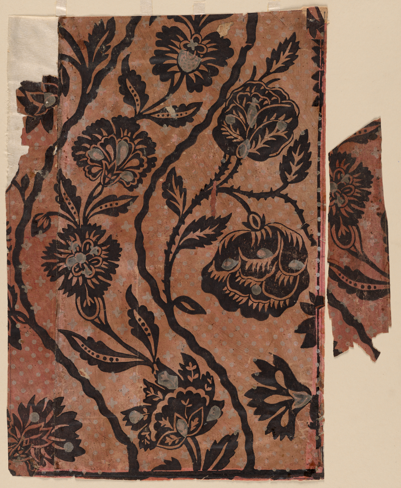 Fragment of vintage repetitive wallpaper depicting silhouetted chrysanthemums, curved vines and leaves. A smaller piece of wallpaper is torn off and placed to the right side of the larger portion.