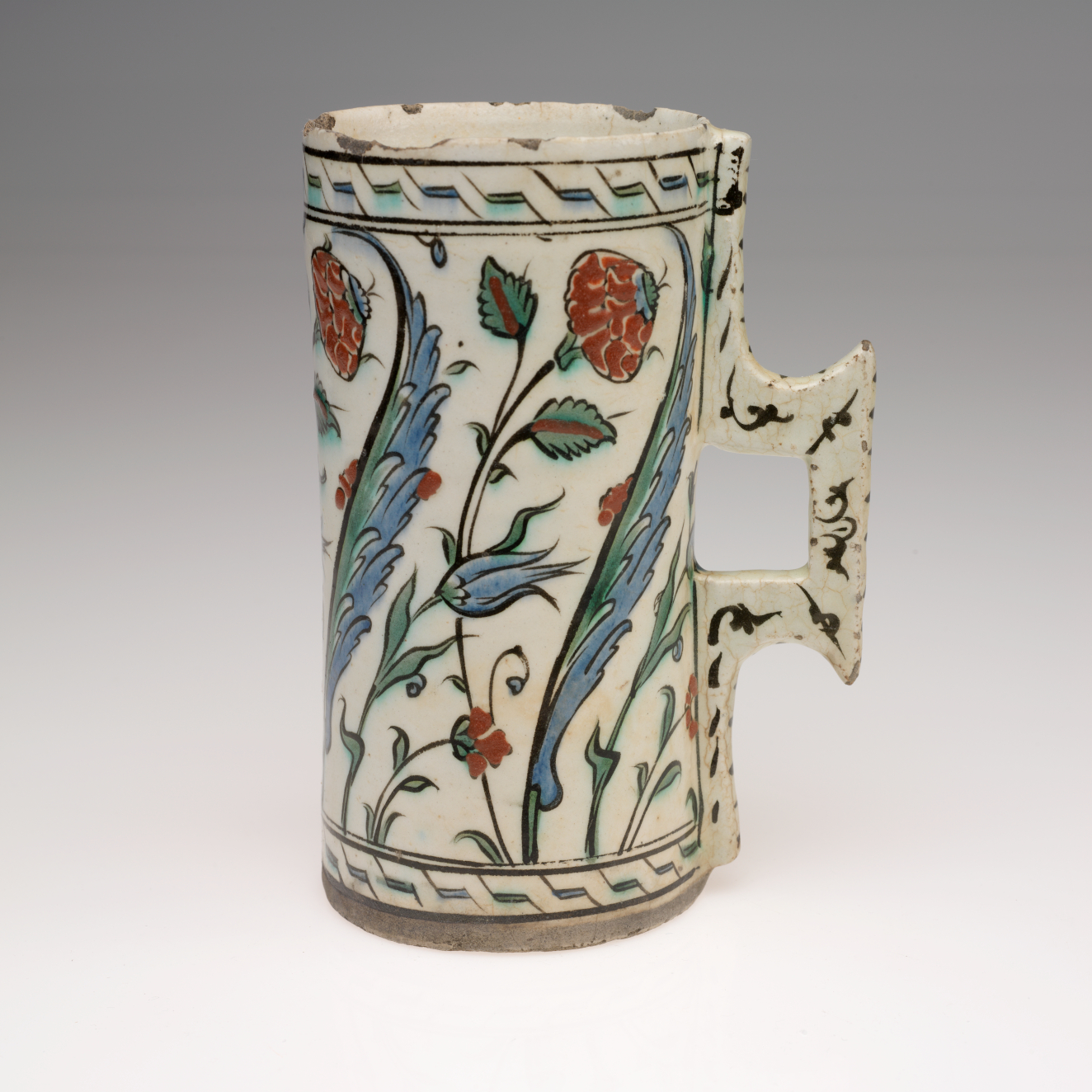 A rounded cream colored vessel with a square handle, decorated with geometric and flower designs in blue, green, and red.