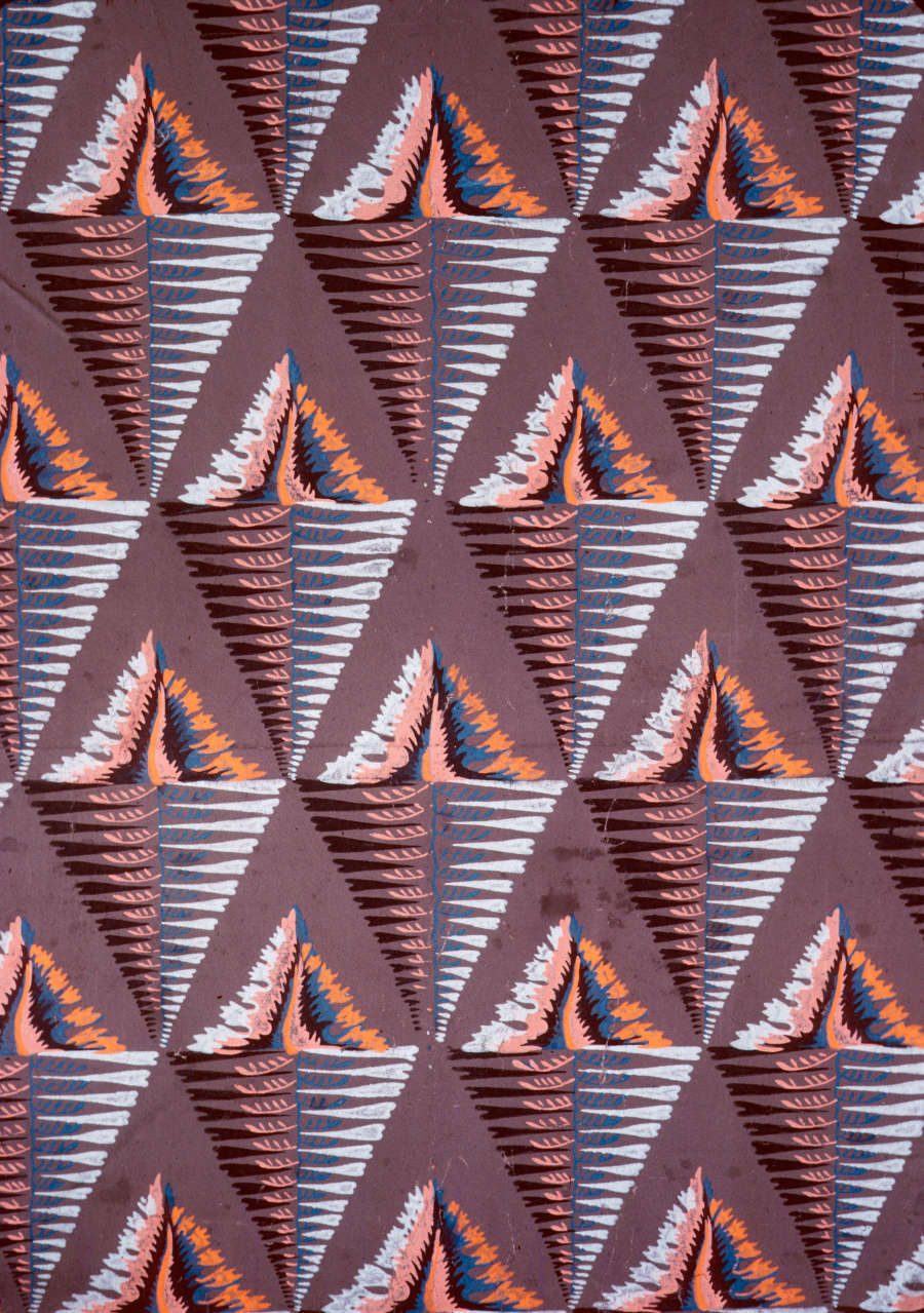 Brown wallpaper with alternate facing triangles repeated horizontally and vertically throughout. The upwards triangle is made of orange and blue blotchy lines  and downwards triangle out of jagged horizontal lines