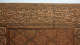A close-up of a carved wooden panel with carved calligraphy along the top edge and geometric star patterns below, framed by decorative borders.