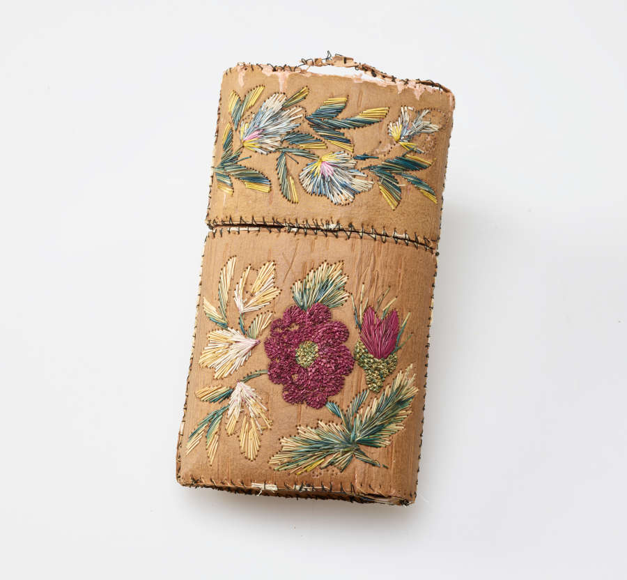 Tan rectangular case. The cap of the case has green, yellow, and blue floral embroidery while the case’s body features pink, yellow, and green floral embroidery.