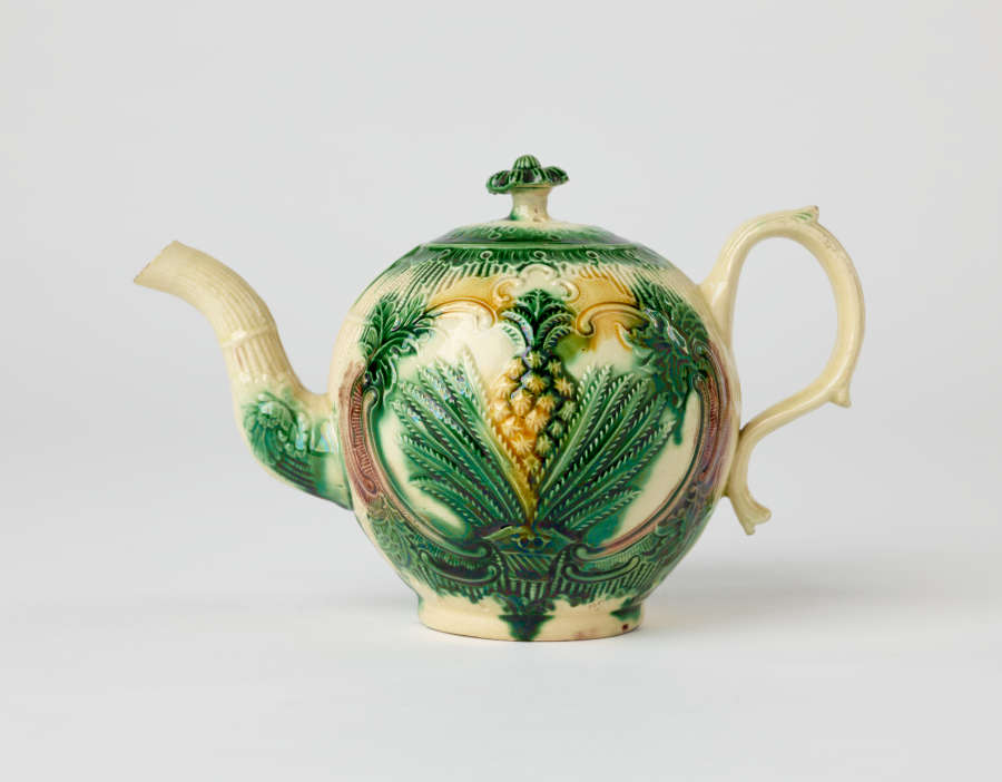 A bulbous teapot with white, green, and yellow floral decorations in the form of a leafy pineapple.