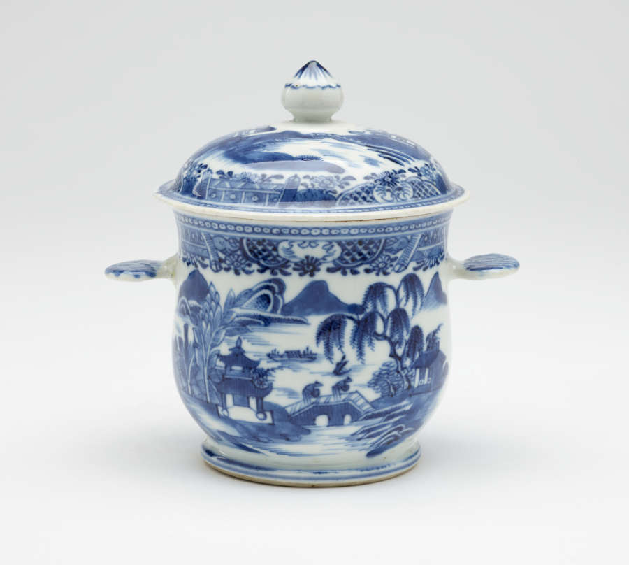 A white bowl with flat handles and lid. The blue decorations are architectural and floral.