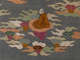 Embroidery of a brown robed figure seated on a peach colored cloud, surrounded by multicolored clouds against a gray background.