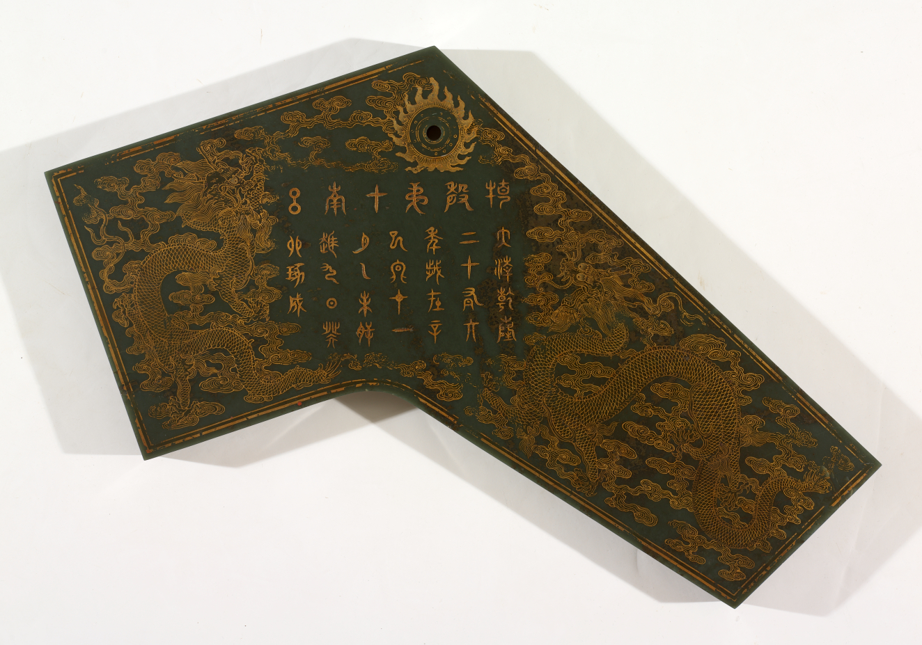 Dark green slab which slopes sharply down to the right, with a dark circle at the top. Features intricate golden embellishments depicting Chinese characters surrounded by dragons above clouds.