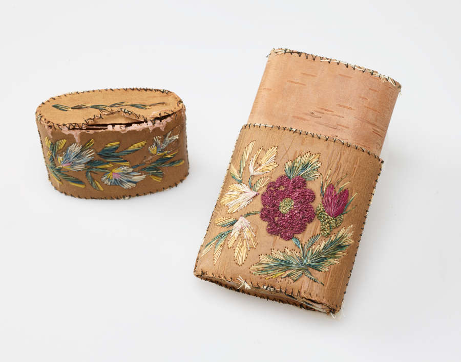 Tan rectangular case with the lid taken off showing that underneath the leather wrapping of the case is another tan surface. The case’s lid and body feature floral embroidery.