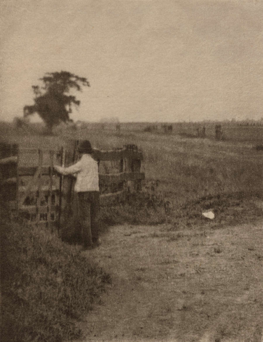 A figure opens a wooden gate near a dirt road in the foreground and a large dark tree in the background.