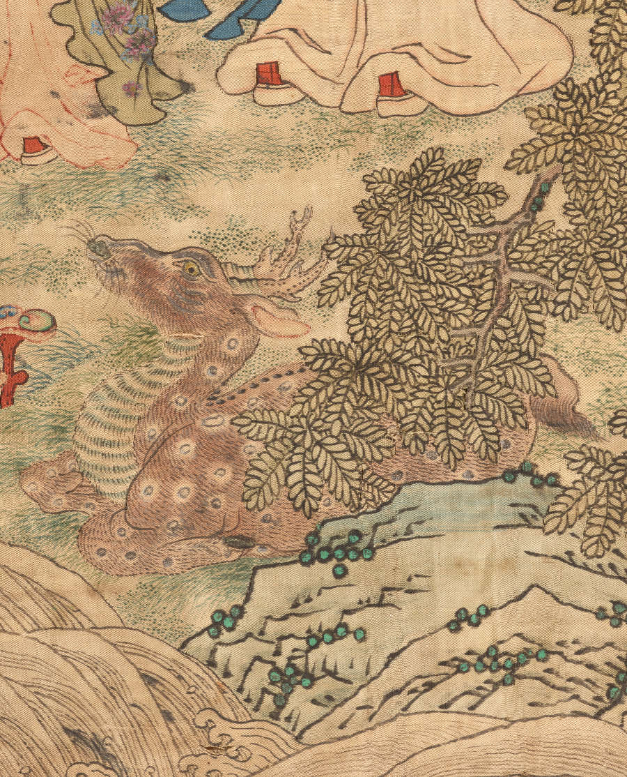 Detail of the scroll showing a seated deer with white spots and horns sitting on grass amongst trees and rocks. 