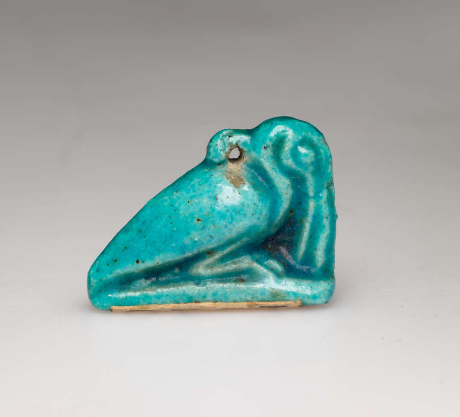 Turquoise amulet of a crouching pelican-like bird with a long beak pointed downwards, head tucked into its neck, where there is a small loop.