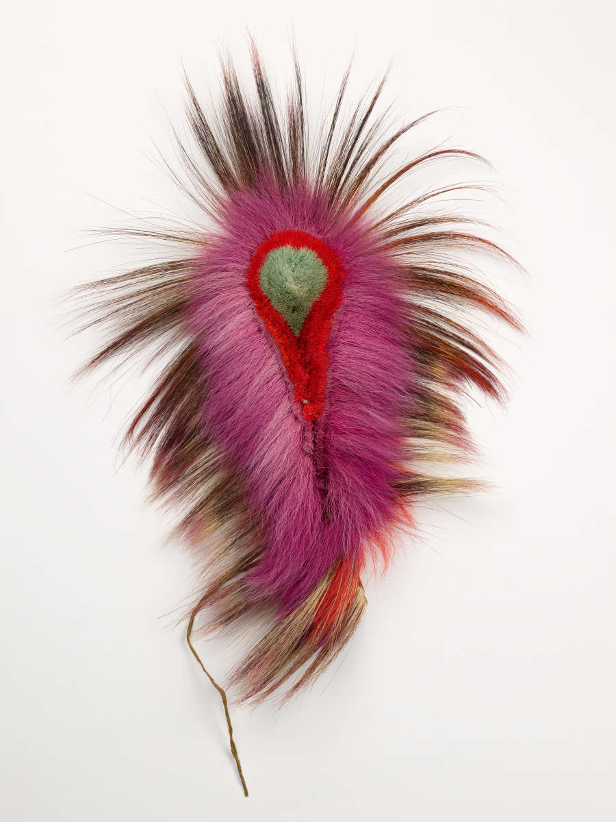 Tear-drop shaped headdress with a red and green interior from which long black, red, and pink gradient feathers emerge with a string at the end.