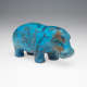 Bright blue ceramic hippopotamus decorated with delicate black-painted floral designs. The rounded body and short legs mimic a hippopotamus’s natural stance. Areas of wear expose golden brown ceramic beneath. 
