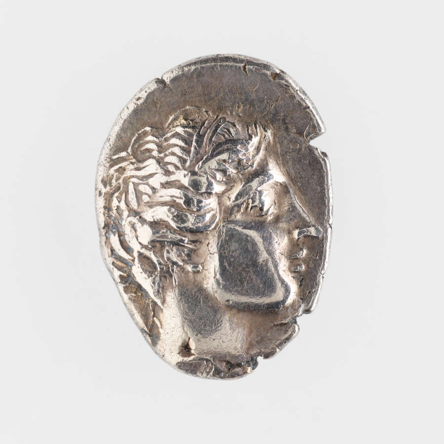 Ovular, rough-edged silver coin embossed with the side profile of a wreathed man with curly hair.