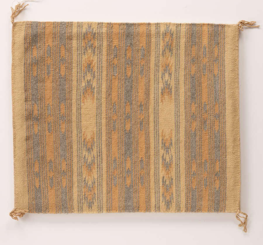 Textile with stripes. Each stripe has a subtle geometric pattern running through it. Palette is peach, tan, and dark blue. Object is square shaped, with small tassels at each corner.