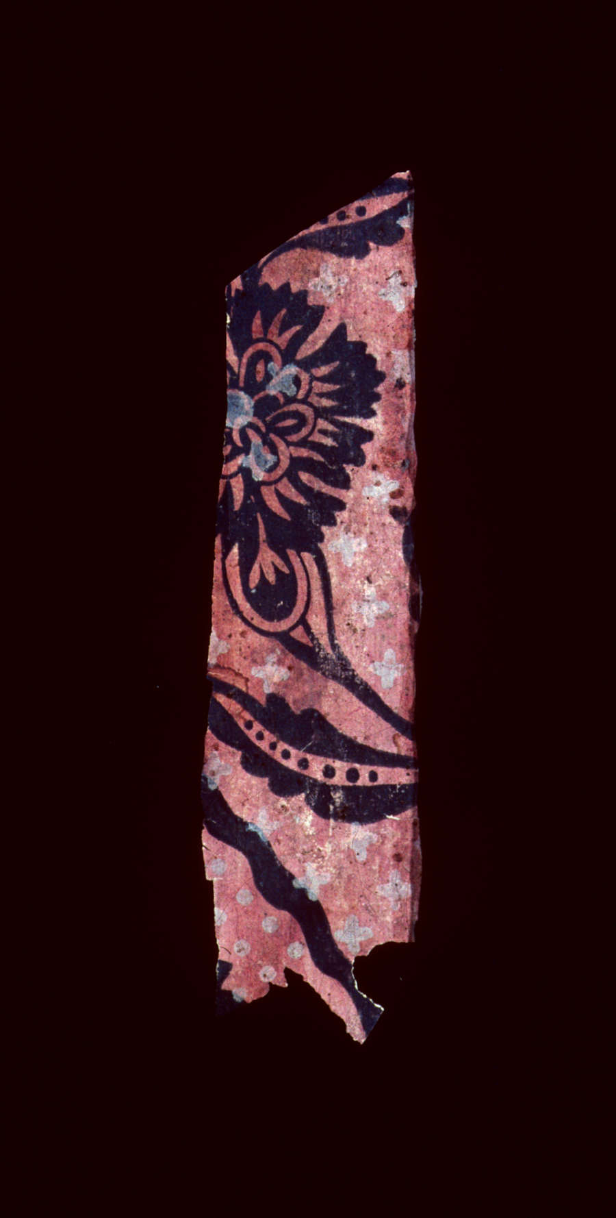 Small fragment of vintage repetitive wallpaper depicting a portion of silhouetted floral motifs set against a pink and white dotted background; blue accents decorate the black silhouettes. 