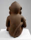 Back of a brown, porous-textured sculpture of a sitting monkey with a long tail held in its right arm. It is propped on a white rectangular platform.