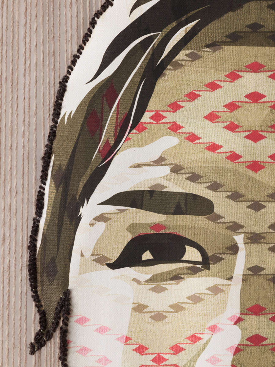 Close-up of the figure's right eye on a woven tapestry. Tiny red and beige diamond shapes with connecting thin lines form a geometric zig-zag pattern across the face.
