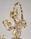 Side view of a silver-robed figure with flowing hair and thin, butterfly-like gold wings holding a draping garland aloft with two cherubs atop a gold orb. 