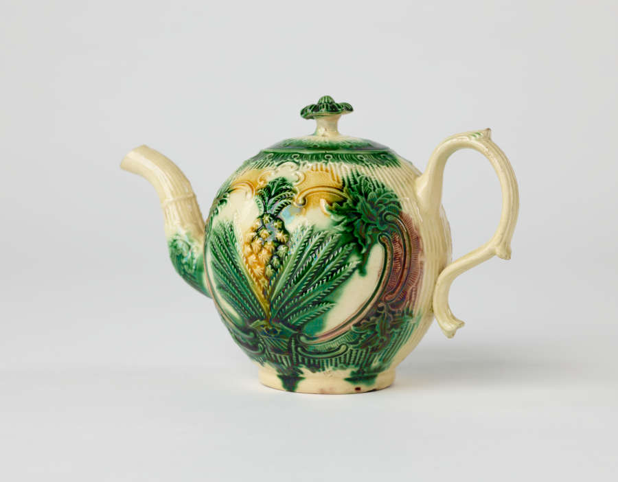 A bulbous teapot with white, green, and yellow floral decorations in the form of a leafy pineapple.