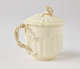  A cream-colored cup with a sculptural swirled handle, and lid with sculpted finial.